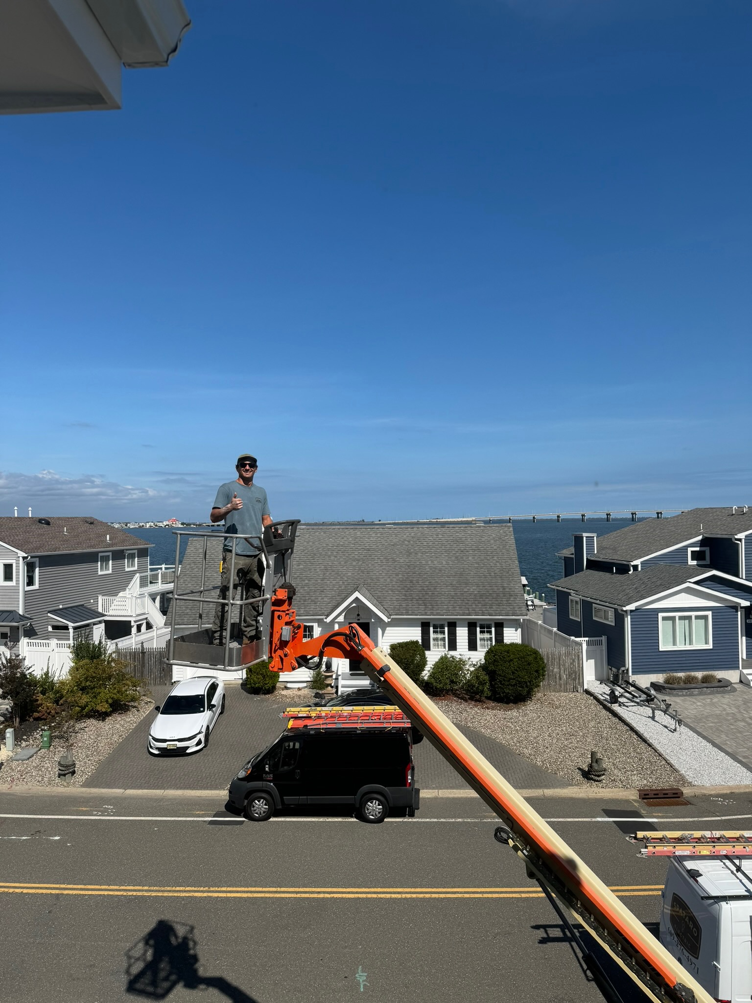 Man standing on a crane with homes and cars behind him.